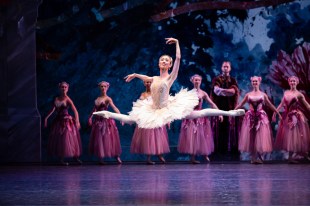 Ballerina Ako Kondo in white tutu in mid leap. Around her are other dancers in pale pink costumes.