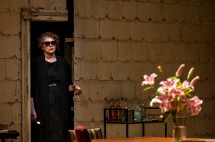 A woman in black, with sunglasses, Pamela Rabe, is standing in a doorframe of a production of 'August. Osage County.'