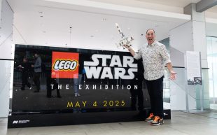 Ryan 'Brickman' McNaught will bring whole new 'LEGO Star Wars: The Exhibition' to Melbourne Museum. A white middle-aged man posing enthusiastically next to a sign with "LEGO STAR WARS THE EXHIBITION MAY 4 2025".