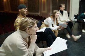 A group of young people in a class room are looking at scripts and off to the right where someone is addressing them off camera. mental health