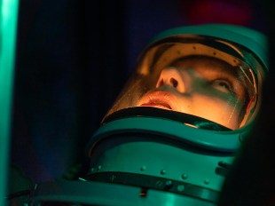 Illuminated face within a space suit looking sky wards. Arts news